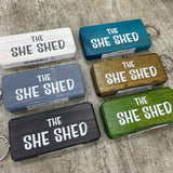 Made in the UK by Giggle Gift Co. Wooden block keyring with white text quote on both sides; 'The She Shed'