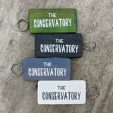 Wooden block keyring with white text quote on both sides; 'The Conservatory'