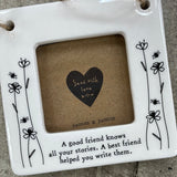 Beautiful white ceramic photo frame with floral detailing up the sides. In the middle is space for a small photo with quote "A good friend knows all your stories. A best friend helped you write them." written underneath. Hung with a jute rope.