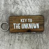 Made in the UK by Giggle Gift Co. Wooden block keyring with white text quote on both sides; 'Key to the Unknown'  brown