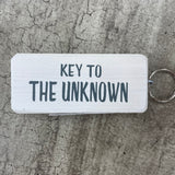 Made in the UK by Giggle Gift Co. Wooden block keyring with white text quote on both sides; 'Key to the Unknown'  white