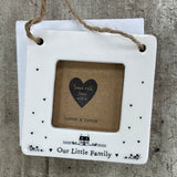 Beautiful white ceramic photo frame with heart detailing up the sides and a cute house illustration. In the middle is space for a small photo with quote "Our Little Family" written underneath. Hung with a jute rope.