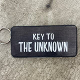 Made in the UK by Giggle Gift Co. Wooden block keyring with white text quote on both sides; 'Key to the Unknown'  black