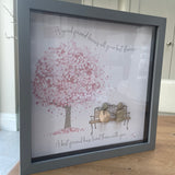Framed Pebble Art - Grey block square frame 27.5cmWith a soft background image of a Tree full of pink flowers and a bench with two pebble friends sitting on it with the quote 'A good friend knows all your best stories... A best friend has lived them with you'