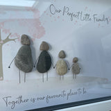 Framed Pebble Art - White block frame 31.5cmWith a soft background image of a Tree with the leaves being pink hearts blowing in the wind and 4 pebble people - 2 adults & 2 children holding hands with the quote 'Our Perfect Little Family... Together is our favourite place to be'