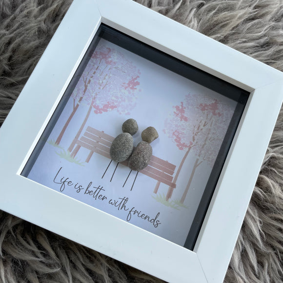 Mini Framed Pebble Art -White block square frame 12.5cm With a soft background image of trees and a bench with two pebble friends sitting together with the quote 'Life is better with friends' 