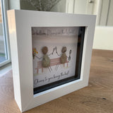 Mini Framed Pebble Art - White block square frame 12.5cmWith a soft background image of a bench and two pebble people sitting on it celebrating with a champagne toast and a bunch of flowers with the quote 'Two Billion Mums in the World.... Cheers to you being the best!'