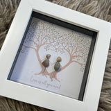 Mini Framed Pebble Art -White block square frame 12.5cmWith a soft background image of two trees full of leaves with two pebble people stood between the trees holding hands with the quote 'Love is all you need'