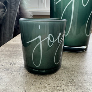 Round Glass Hurricane Vase in a Deep Green/Grey colour
Has the word 'Joy' in a scrolling text on both sides
Available in 2 sizes; Small H8cm &amp; Large H18cm&nbsp;