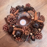 Round t-light centrepiece with layers of pinecones, cinnamon sticks, foliage in rich warm colours 24cm