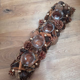 Table centrepiece with pinecones, cinnamon sticks, foliage in rich warm colours and 4 t-light cups integrated 51cm