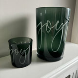 Round Glass Hurricane Vase in a Deep Green/Grey colour
Has the word 'Joy' in a scrolling text on both sides
Available in 2 sizes; Small H8cm &amp; Large H18cm&nbsp;