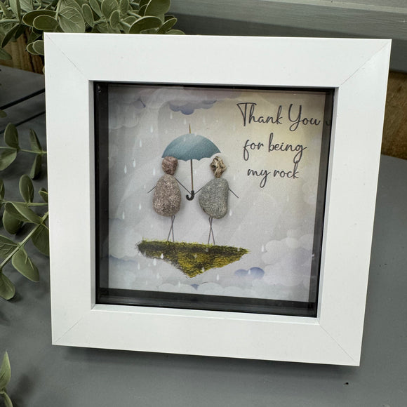 Mini Framed Pebble Art - White block square frame 12.5cm
Two pebble people stood on a rock holding an umbrella with it raining and surrounded by clouds
Quote - 'Thank you for being my rock'