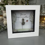 Pebble Art by La De Da Living&nbsp;

Award winning keepsake gifts - Handmade in the Cotswolds&nbsp;

Mini Glitter Framed Pebble Art - White block square frame 12.5cm
Image - Pebble person holding flowers and two blossom glitter trees either side with flower beds &amp; butterflies..&nbsp;
Quote - 'You are one in a million'