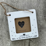 Beautiful white ceramic photo frame with heart detailing up the sides and a cute house illustration. In the middle is space for a small photo with quote "Our Little Family" written underneath. Hung with a jute rope.