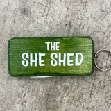Made in the UK by Giggle Gift Co. Wooden block keyring with white text quote on both sides; 'The She Shed'  green