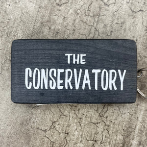 Wooden block keyring with white text quote on both sides; 'The Conservatory' 