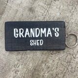 Made in the UK by Giggle Gift Co. Wooden block keyring with white text quote on both sides; 'Grandma's Shed'  black