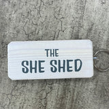 Made in the UK by Giggle Gift Co. Wooden block keyring with white text quote on both sides; 'The She Shed'  white with grey text