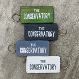 Wooden block keyring with white text quote on both sides; 'The Conservatory' 