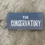 Wooden block keyring with white text quote on both sides; 'The Conservatory'  Grey