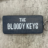 Made in the UK by Giggle Gift Co. Wooden block keyring with white text quote on both sides; 'The Bloody Keys' Black
