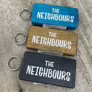 Made in the UK by Giggle Gift Co. Wooden block keyring with white text quote on both sides; 'The Neighbours' 