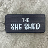 Made in the UK by Giggle Gift Co. Wooden block keyring with white text quote on both sides; 'The She Shed'  black