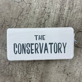 Wooden block keyring with white text quote on both sides; 'The Conservatory'  White