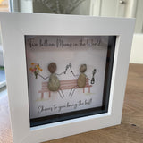 Mini Framed Pebble Art - White block square frame 12.5cmWith a soft background image of a bench and two pebble people sitting on it celebrating with a champagne toast and a bunch of flowers with the quote 'Two Billion Mums in the World.... Cheers to you being the best!'