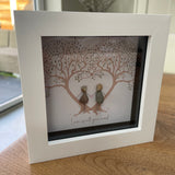 Mini Framed Pebble Art -White block square frame 12.5cmWith a soft background image of two trees full of leaves with two pebble people stood between the trees holding hands with the quote 'Love is all you need'