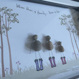 Framed Pebble Art - White block frame 31.5cmThe background image is tall trees on both sides with wild flowers growing and 3 Pebble people wearing colourful wellies holding hands with the flowers with the quote 'Where there is family...there is love'