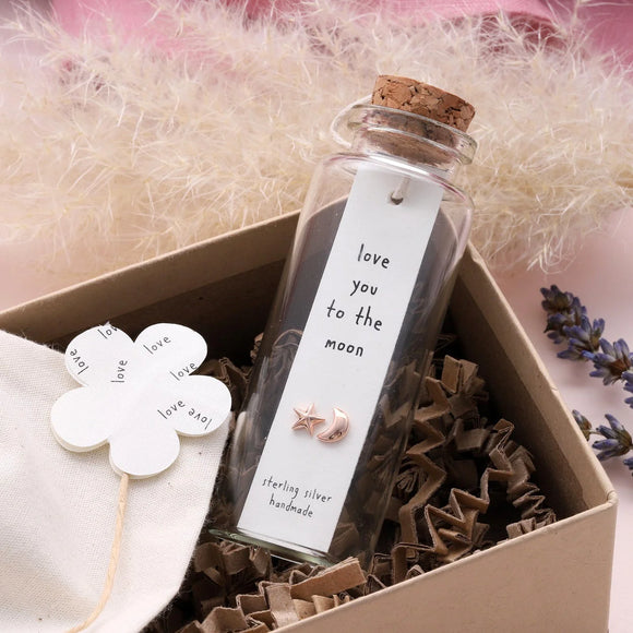 Sweet asymmetrical stud earrings - one shaped like a star and the other a moon - presented in a message bottle on a card that reads 