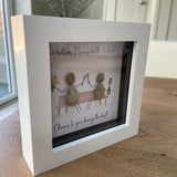 Mini Framed Pebble Art - White block square frame 12.5cmWith a soft background image of a bench and two pebble people sitting on it celebrating with a champagne toast and a bunch of flowers with the quote 'Two Billion Mums in the World.... Cheers to you being the best!' 
