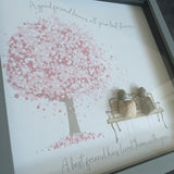 Framed Pebble Art - Grey block square frame 27.5cmWith a soft background image of a Tree full of pink flowers and a bench with two pebble friends sitting on it with the quote 'A good friend knows all your best stories... A best friend has lived them with you'