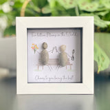 Mini Framed Pebble Art - White block square frame 12.5cmWith a soft background image of a bench and two pebble people sitting on it celebrating with a champagne toast and a bunch of flowers with the quote 'Two Billion Mums in the World.... Cheers to you being the best!'